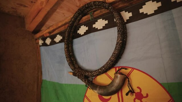 Culture and tradition. View of a Mapuche aborigine musical instrument, Ñolkin that belongs to the family of the trumpets and is made with wood and animal guts. The Mapuche flag hanging in the wall. 