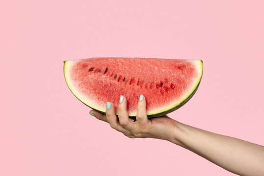 Female hand holding slice of watermelon on pink background