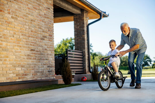 Grandfather is teaching his grandson riding a bicycle in backyard.