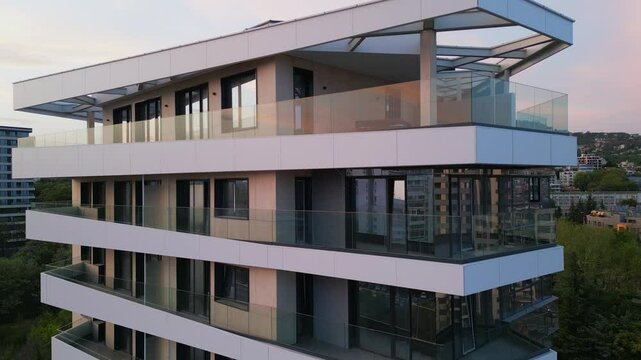 Aerial drone shot of a modern residential building facade with beige panels and white balconies, highlighting clean architectural lines and contemporary urban design