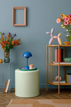 Stylish interior vignette featuring a blue lamp, fresh flowers in a vase, and playful decorative elements on a minimalistic shelf