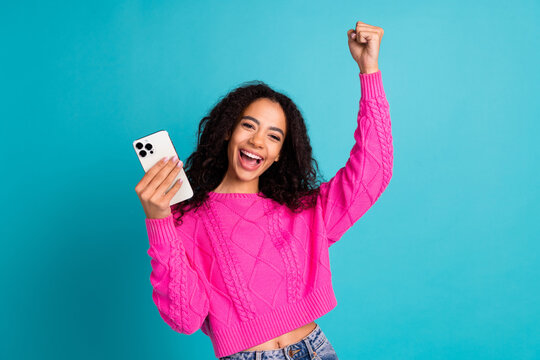 Photo portrait of attractive teen girl hold device winning dressed stylish pink clothes isolated on aquamarine color background