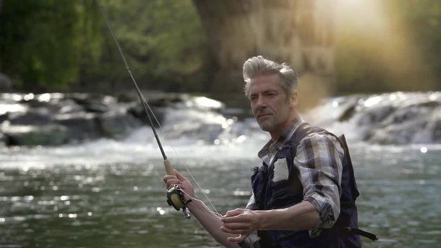 Slow motion of mature man fly fishing in river