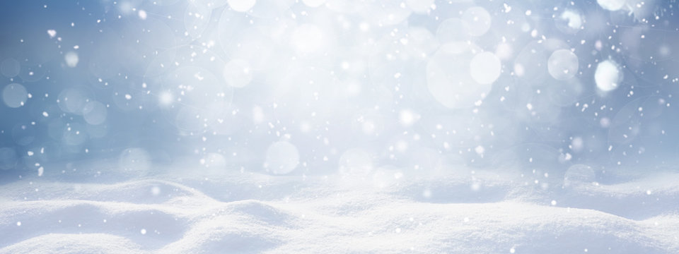 Winter snow background with snowdrifts, with beautiful light and snow flakes on the blue sky, beautiful bokeh circles, banner format, copy space.