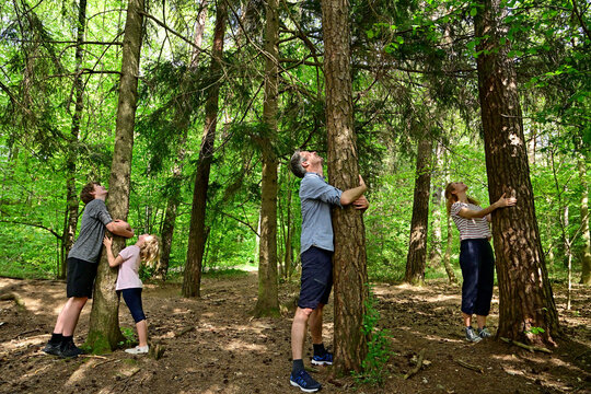 Parents and children embracing tree while standing in forest