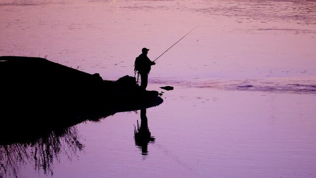 Silhouette of angler spin fishing at river shore in the evening, outdoor hobby healthy activity.