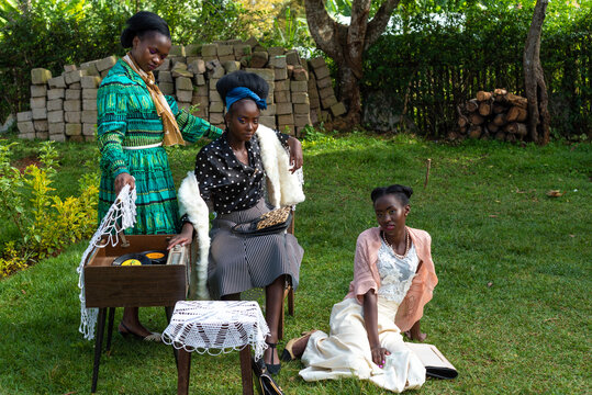 Portrait of three young African women posing with an old record player in front of rural house 