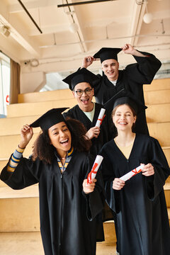 Diverse group of students in graduation gowns and caps smiling for a group photo indoors.