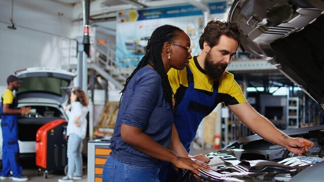 Certified engineers in auto repair shop working together on fixing car, discussing best options. Specialist and colleague collaborating on servicing broken vehicle, checking for damaged components