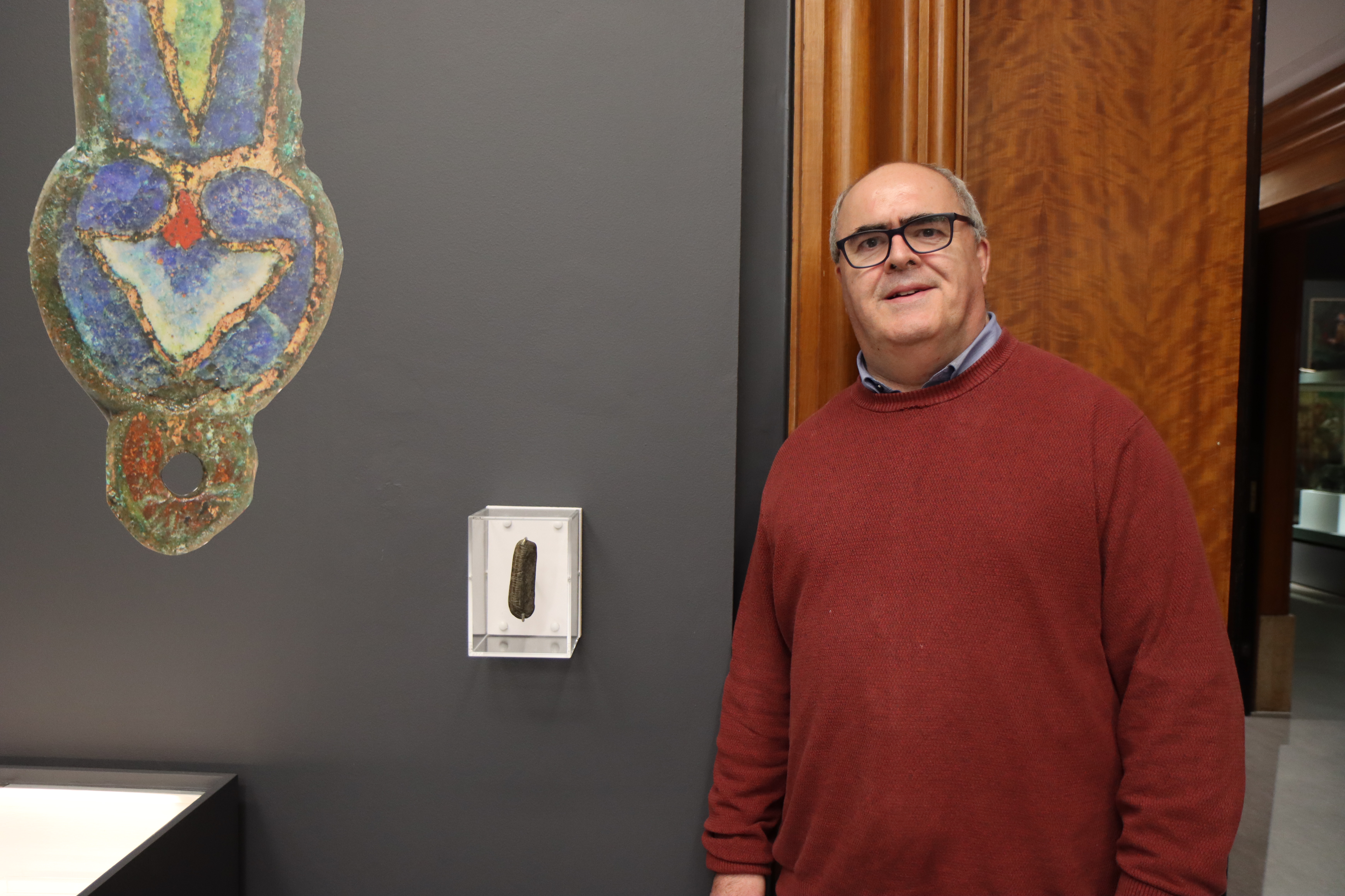 Man in red sweater standing next to stone in display case