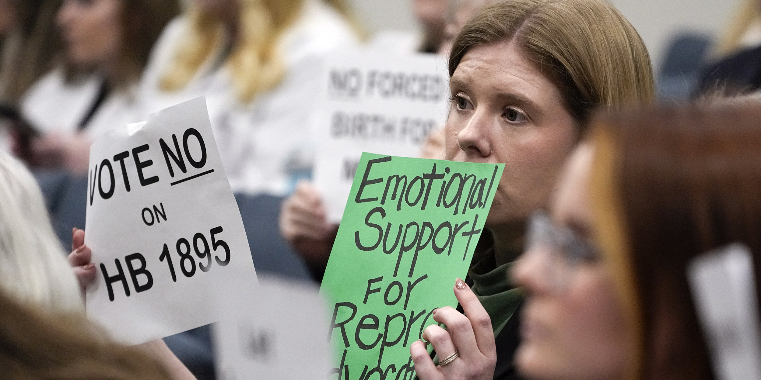 Kay Cook holds signs during a House Health Committee meeting against HB1895, Wednesday, Feb. 21, 2024, in Nashville, Tenn. The bill would create the criminal offense of abortion trafficking of a minor. (AP Photo/George Walker IV)