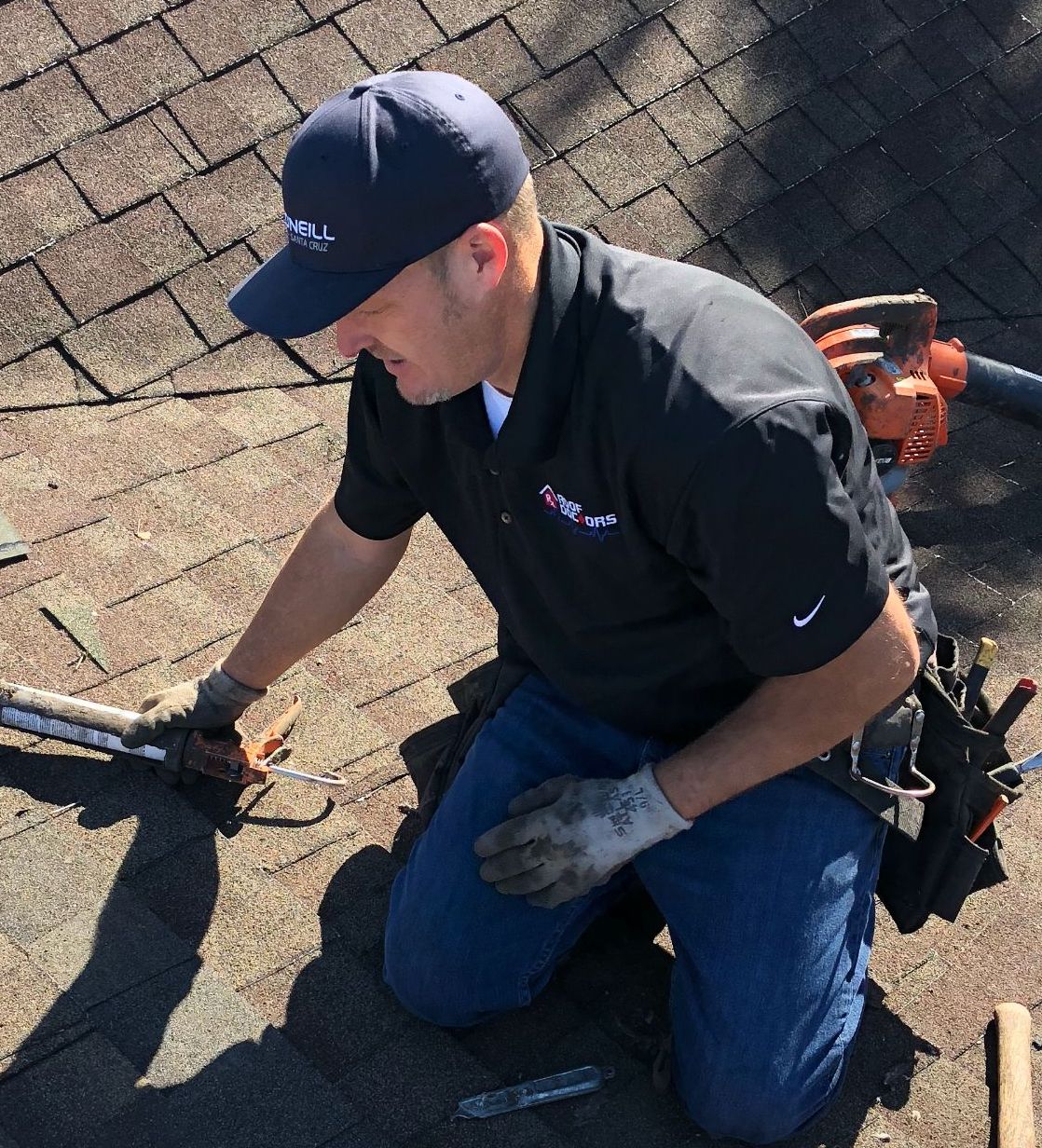 Worker on shingle roof repairing the roof with roof sealant