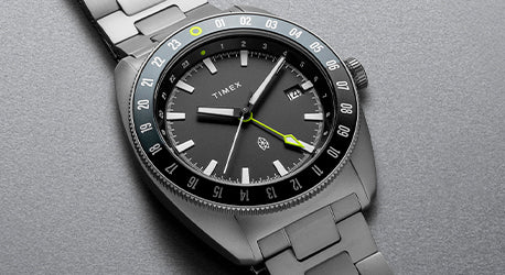 Black Bezel watch on a grey strap laying across a grey background.