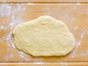 Overhead shot of challah dough that has been rolled into an oval shape on top of a floured cutting board.