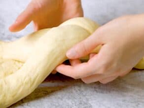 Two hands lifting braided challah dough from beneath.