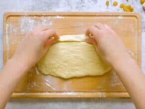 Overhead shot of two hands beginning to roll the challah dough into a strand.