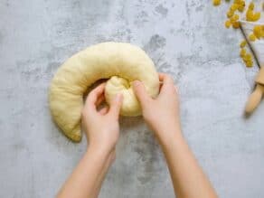 Overhead shot of two hands rolling a strand of challah dough into a coil shape, known as a turban challah.