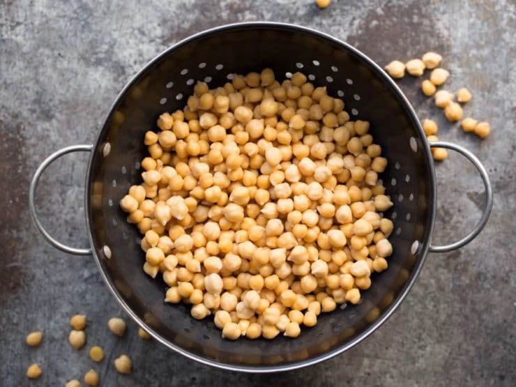 Overhead shot of cooked chickpeas in colander on a grey background.