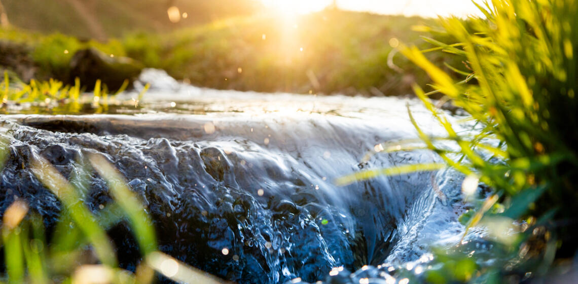 A spring river flowing over rocks creating a small waterfall, the sun is rising in the background