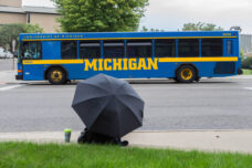 A commuter blocks the light rain as she waits for the next bus.