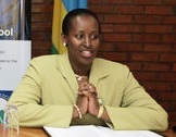 Jeannette Kagame shown sitting at a desk at a public event, wearing a yellow jacket