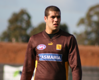 Portrait photography of short-haired man wearing mostly brown, and yellow long-sleeved shirt with TASMANIA imposed on the front.