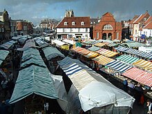 Brightly coloured canvas tops of many market stalls in a town setting.