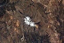 A roughly pear-shaped ice area, from which valleys emanate, lies within a multicolored landscape, as seen from a satellite image.