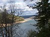 A large lake between two hilly shores, seen through trees in the foreground