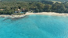 An aerial view of a beach in St Croix, showing a light blue ocean, sandy beach, and green trees