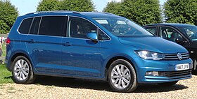 Front-three-quarter view of a five-door car with a raised roofline, flush headlights, front foglamps, door mirrors with integrated turning indicator lights, alloy wheels, and bars for attaching a roof rack