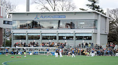 A grey coloured function centre with glass windows. Spectators and an interchange bench are in front of the structure.