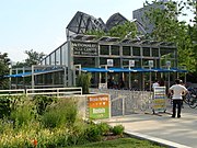 A glass building beyond landscaping with signs pointing to downstairs facilities and a sign reading "McDonald's Cycle Center 239 E. Randolph" with people in the building and in front of it