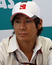 A portrait of a man in his mid-20s wearing a white T-shirt and baseball cap with the logo of the Sauber Formula One team looking to the right of the camera