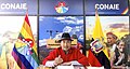 A man in a fedora and poncho, seated in front of logos for CONAIE and the flags of CONAIE and Ecuador