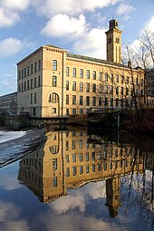 A stone factory stands against a vivid blue sky, its reflection mirrored in the waters below.