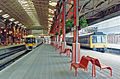 The full set: red lamp posts, red benches, electro-mechanical clock & two trains in NSE livery.