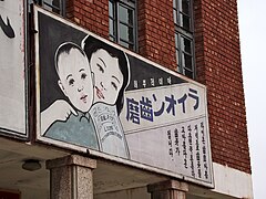 Photo d'un panneau publicitaire. Deux visages d'enfants stylisés et souriants occupent la moitié du cadre. L'autre moitié est occupée par le nom du dentifrice et par un texte explicatif.