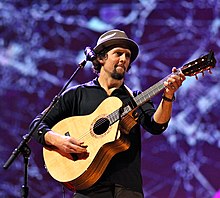 A Caucasian man wearing a bucket hat strums a guitar