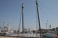 In the foreground of this harbor scene is visible the plastic-wrapped top of a ship hull. The ship has two tall masts.