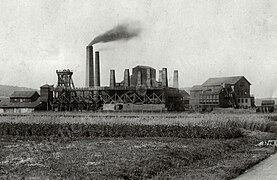 Anciens bâtiments industriels en bois, pierre et brique surmontées de multiples cheminées.