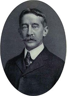 Formal photo of man in suit and tie with full head of hair and handlebar moustache