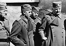 A black and white photograph of four older males in military uniform wearing peakless caps