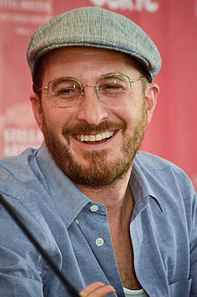 Darren Aronofsky kneeling while holding a microphone