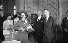 photo en noir en blanc ; le roi et la reine, chapeautée et munie d’un bouquet de fleurs, sont particulièrement souriants.