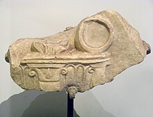 Photograph of a fragment of white marble sculpture, showing a tripod sculpted in bas-relief.