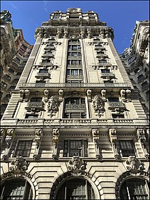 Detail of the southern facade of the Ansonia. The facade is made of white limestone and contains three windows on every story. There are ironwork balconies or grilles in front of each window. The lower stories of the facade contain ornate limestone decoration, including a balustrade.