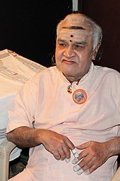 Photograph of an old man sitting in a chair.