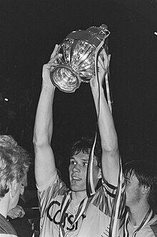 Photograph of some Ajax team players with one of them holding the trophy over his head