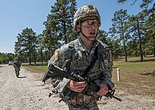 A tired-looking soldier in full uniform, running with a gun during a competition